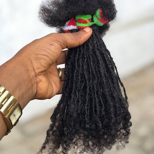 May include: A bundle of black dreadlocks hair extensions with red, white, and green bands.