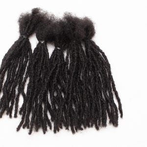 Peut inclure: Un ensemble de quatre extensions de cheveux en dreadlocks noires. Les dreadlocks sont longues et épaisses, et elles sont attachées ensemble en haut.