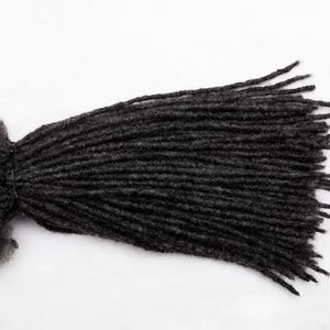 Op de afbeelding: Een bundel donkergrijze dreadlocks, stevig vastgebonden aan één uiteinde, uitwaaierend naar individuele strengen. De dreadlocks hebben een getextureerd uiterlijk, tegen een effen witte achtergrond.