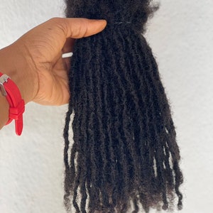 Puede incluir: Un paquete de rastas de color marr&oacute;n oscuro, bien atadas en la parte superior. Las rastas individuales tienen textura y cuelgan hacia abajo, mostrando un peinado natural. El cabello parece reci&eacute;n peinado y listo para usar.