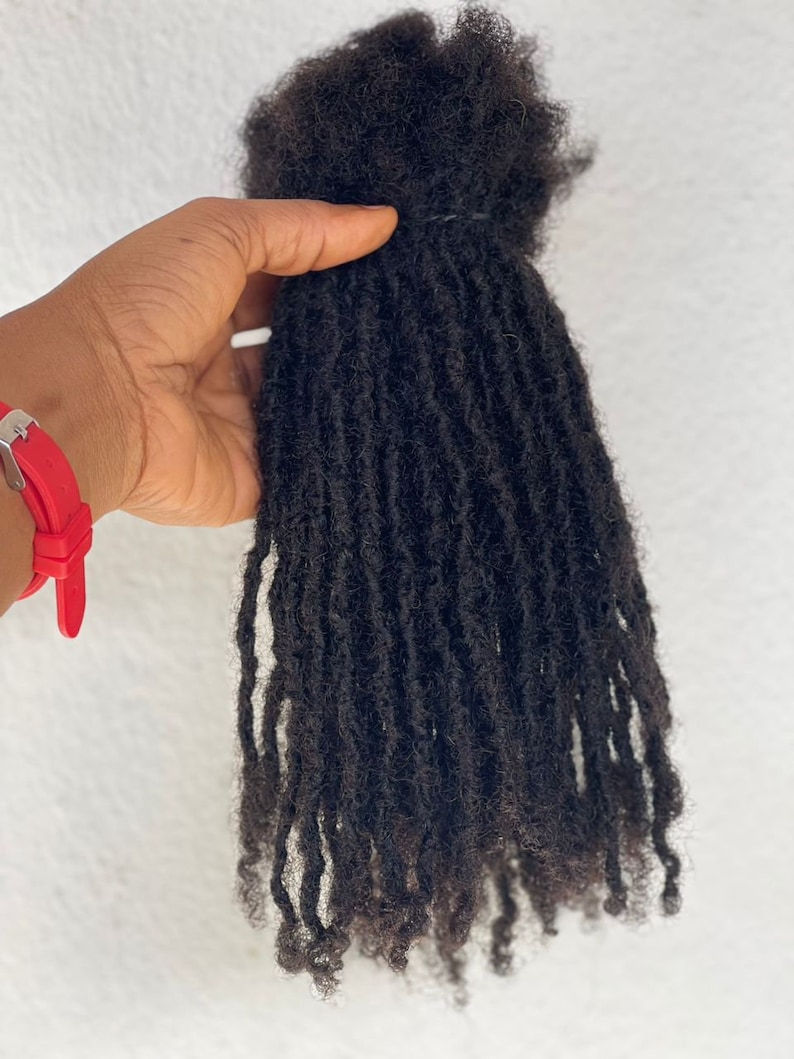 Puede incluir: Un paquete de rastas de color marr&oacute;n oscuro, bien atadas en la parte superior. Las rastas individuales tienen textura y cuelgan hacia abajo, mostrando un peinado natural. El cabello parece reci&eacute;n peinado y listo para usar.