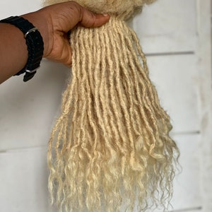 May include: A bundle of blonde human hair dreadlocks. The dreadlocks are long and wavy, with a light blonde color.