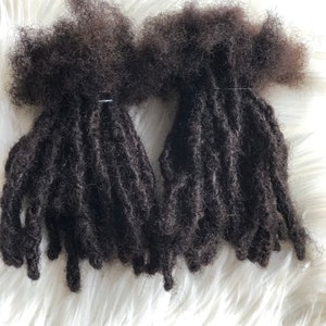 May include: Two bundles of dark brown human hair dreadlocks. The dreadlocks are tied together with a rubber band.