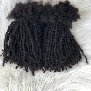 May include: Dark brown dreadlock extensions, bundled together. The extensions are made of a textured material and are arranged on a white, fluffy surface. The dreadlocks are a deep, natural color.