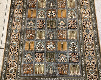 May include: A beige rug with a detailed floral pattern in shades of green, brown, and black. The rug has a central design of repeating squares with intricate floral motifs. The rug has a fringe border.