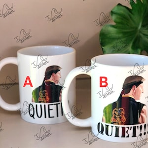 May include: Two white ceramic mugs with a handle, each featuring a design of a man in a karate uniform. One mug says "QUIET" and the other says "QUIET!!!". The mugs are decorated with a colorful illustration.