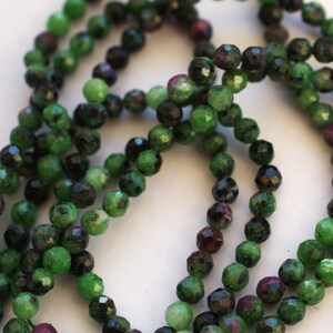 May include: A strand of green, black, and pink gemstone beads. The beads are faceted and have a round shape.