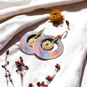 May include: A pair of iridescent round earrings with a gold wire spiral design. The earrings are on a white fabric background.