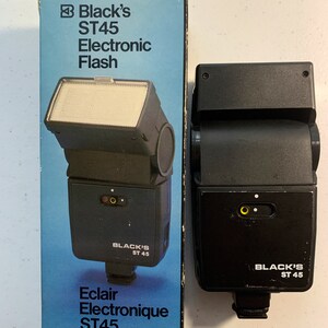 May include: Black's ST45 Electronic Flash in its original box. The flash is black with a silver reflector and has a black and white label that reads "Black's ST45". The box is blue and white and has the text "Black's ST45 Electronic Flash" and "Eclair Electronique ST45".