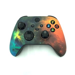 May include: A black Xbox controller with a nebula-like design featuring shades of orange, yellow, green, and blue.