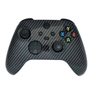May include: A black Xbox controller with a carbon fiber design. The controller has the standard buttons, including A, B, X, and Y, which are colored green, red, blue, and yellow, respectively.