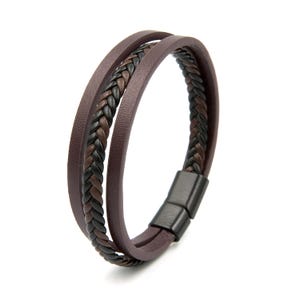 Può includere: Un bracciale a più fili caratterizzato da una fascia in pelle marrone scuro liscia abbinata a un cordino intrecciato composto da fili neri e marroni alternati. Il bracciale è fissato con una chiusura magnetica rettangolare nero opaco.