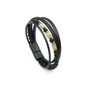 Puede incluir: Una pulsera de varias hebras con cordones de cuero negro, una hebra de cuero trenzado y una fila de cuentas negras mate. El diseño incluye una hebra central con cuentas de piedra clara alternadas y pequeños espaciadores de metal dorado.