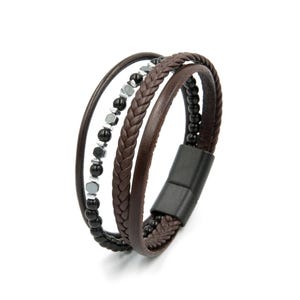 May include: A multi-strand bracelet featuring a smooth brown leather cord, a braided brown leather strap, and a strand of black beads interspersed with metallic hexagonal spacers, secured by a matte black cylindrical magnetic clasp.
