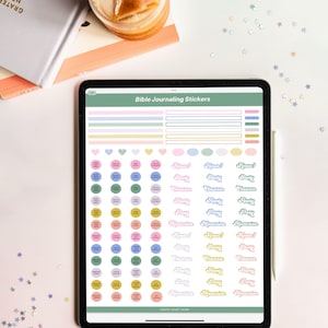 May include: A digital tablet screen displaying a sheet of printable Bible journaling stickers. The stickers feature various pastel colors and designs, including circles, hearts, and words like "Amen!" and "Memorize". The text "Bible Journaling Stickers" is at the top of the screen.