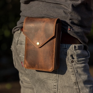 May include: A brown leather fanny pack with a flap closure and a brass button. The pack is worn on a person's waist.