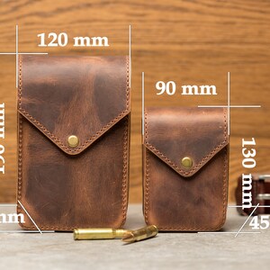 May include: Two brown leather phone cases with a flap closure and a brass button. The larger case measures 120 mm by 190 mm and the smaller case measures 90 mm by 130 mm. The cases are shown on a wooden surface with bullets and a belt.