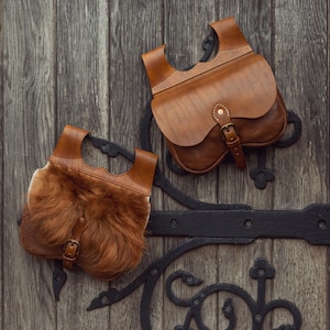 May include: Two brown leather bags with a flap closure and a buckle. One bag has a brown fur lining. The bags are hanging on a wooden door with black metal hardware.