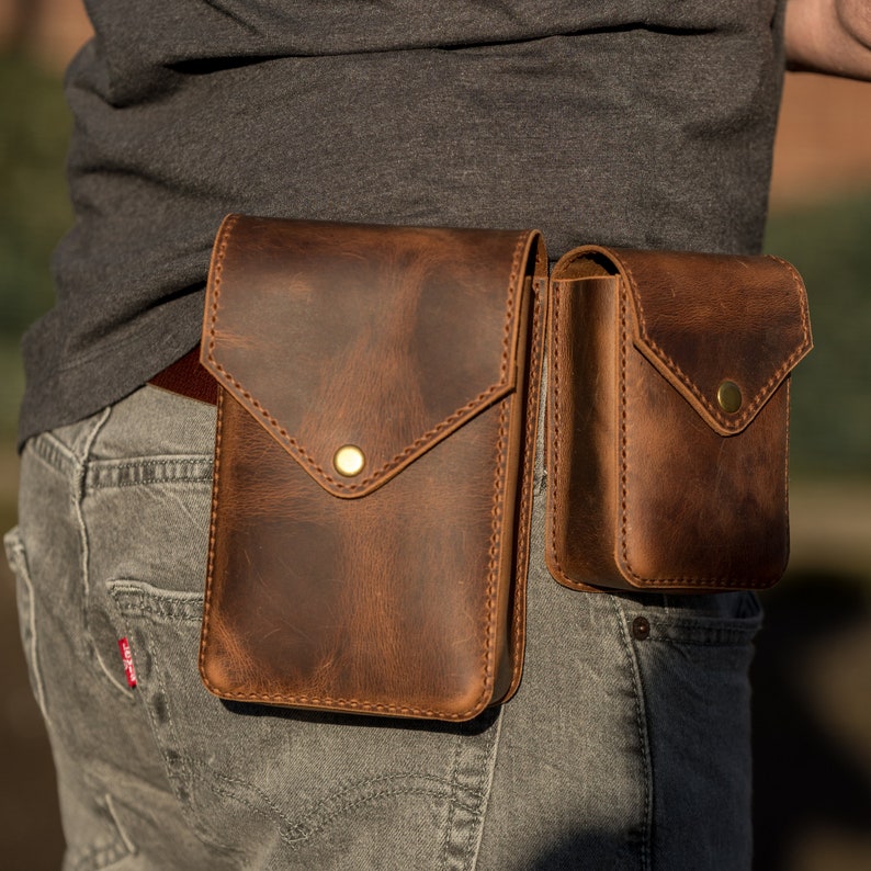 May include: A brown leather belt with two attached pouches. The larger pouch has a flap with a gold button closure. The smaller pouch has a flap with a gold button closure.