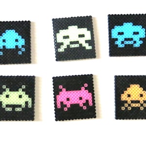 Peut inclure: Six porte-clés carrés en pixel art représentant des envahisseurs spatiaux de différentes couleurs. Les porte-clés sont noirs avec un contour blanc et présentent des envahisseurs spatiaux de différentes couleurs en bleu, bleu clair, vert, rose, orange et jaune.