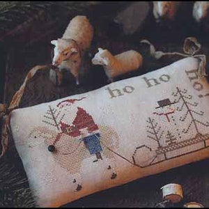 May include: A cross-stitched Christmas pillow with Santa Claus and a snowman design. The pillow features the words "ho ho ho!" and a Christmas tree. The image also includes small sheep figurines and the text "SNOW FOR CHRISTMAS".