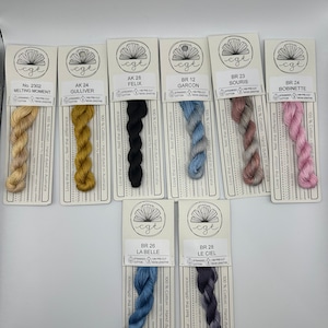 May include: Assortment of 10 skeins of embroidery floss in various colors, including beige, yellow, black, blue, pink, and gray. Each skein is labeled with a color name and a number. The floss is 100% cotton and hand-dyed in Australia.