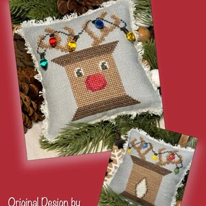 May include: A light blue pillow with a brown and white reindeer design. The reindeer has a red nose and is wearing a string of colorful lights. The pillow has a frayed edge.