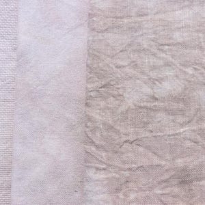 May include: A silver treble clef charm rests on a light purple fabric with a textured weave. The fabric transitions to a lighter shade and then to a textured, crinkled fabric in a muted, dusty rose color. The image showcases a textile design.