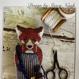 May include: Cross-stitch pattern for a red fox wearing a blue and white striped apron and carrying a small bag. The pattern is titled "Animal Crackers British Series + Reynard +" and is designed by Stacy Nash.