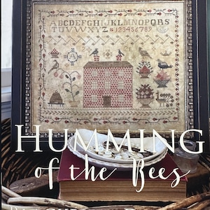 May include: A cross-stitch pattern titled "Humming of the Bees" by Blackbird Designs. The pattern features a red brick house with a chimney, a birdhouse, and a variety of flowers and birds. The alphabet and numbers are included in the pattern.