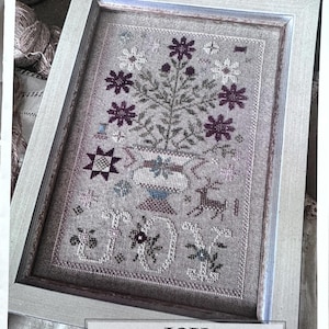 May include: A framed cross-stitch pattern with a floral design in shades of purple, white, and brown. The pattern is titled "JOY" and is a 2025 Nashville Exclusive by Shakespeare's Peddler.