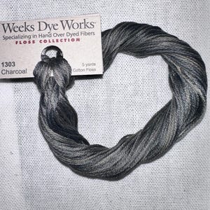 May include: A skein of charcoal-colored cotton floss from Weeks Dye Works, labeled "1303 Charcoal." The floss is 5 yards long and is displayed on a white, textured surface. The packaging includes the text "FLOSS COLLECTION."