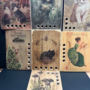 May include: Set of six wooden plaques with various images printed on them. The images include a group of dogs, a woman with long hair, a cat, a Christmas tree, a black cat, and a woman in a green dress. Each plaque has a row of holes along the bottom edge.