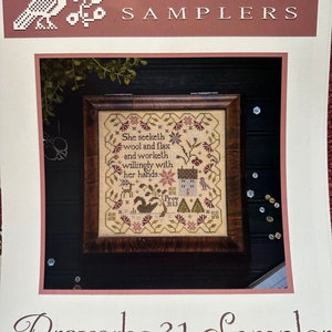 May include: A cross-stitch sampler pattern featuring a verse from Proverbs 31:13, "She seeketh wool and flax, and worketh willingly with her hands." The sampler is framed in a dark wood frame and includes a small house, trees, and birds.