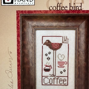May include: Wee One Coffee Bird cross stitch pattern by Heart in Hand needleart. The pattern features a red bird standing on one leg with a coffee pot and a cup of coffee. The text "Coffee" is stitched below the bird.