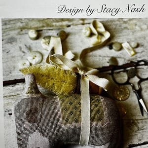 May include: Cross-stitch pattern for a gray and green animal cracker with a yellow brush tail and a white ribbon. The pattern is titled "Animal Crackers Series + Millie + Design by Stacy Nash".