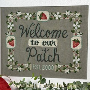 May include: Cross-stitch pattern featuring a welcome sign with a strawberry border. The sign reads "Welcome to our Patch Est. 2000".