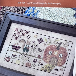 May include: Cross-stitch sampler in a dark wood frame, featuring a pumpkin house, squirrel, and the text "Tommy's Pumpkin Patch." The design includes floral and autumnal elements, with a muted color palette of browns, greens, and purples.