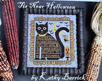 May include: A framed cross-stitch design featuring a black cat with a yellow collar and the text 'Tis Near Halloween. When witches go riding & black cats are seen. The moon laughs & whispers 'tis near Halloween. by Kathy Barrick.