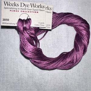 May include: A skein of Weeks Dye Works cotton floss in a deep purple hue. The floss is labeled "3850 Williamsburg R" and is 5 yards in length. The label reads "Specializing in Hand Over Dyed Fibers" and "FLOSS COLLECTION".