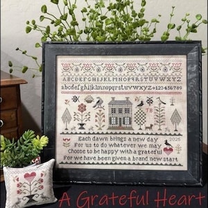 May include: A framed cross-stitch sampler featuring an alphabet, numbers, a house, birds, trees, and the text: Each dawn brings a new day, For us to do whatever we may, Choose to be happy with a grateful, For we have been given a brand new start 2025.