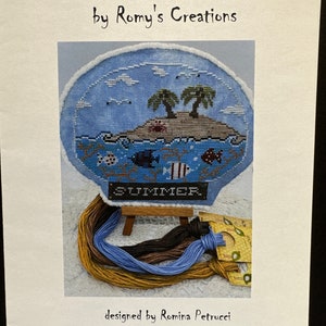 May include: Cross stitch pattern for a snow globe with a summer scene. The snow globe features a blue sky, two palm trees, a small island, and the word "SUMMER" in the center. The pattern is designed by Romina Petrucci.