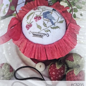 May include: A cross-stitch design featuring a blue bird, strawberries, and green leaves on a white background, set in a red basket with a ruffled edge. The image includes the text "Strawberries & Stripes" and the design number #CS235.