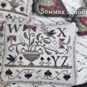 May include: Cross-stitch sampler pillow with floral and letter designs. The pillow features the letters W, X, Y, and Z, along with a floral arrangement in a vase. The text "Summer Schoolhouse" and "Lesson #4" are also visible.