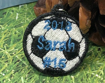 May include: A white and black soccer ball with blue embroidery. The ball has the text "2013 Sarah #15" embroidered on it.