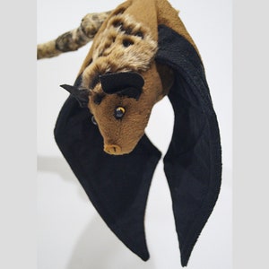 May include: A brown and black plush bat with large black wings. The bat has a furry face with black eyes and a small nose.