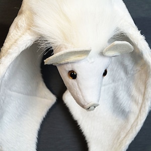 May include: White plush bat with large, furry wings and brown eyes. The bat is hanging upside down with its head facing the camera.