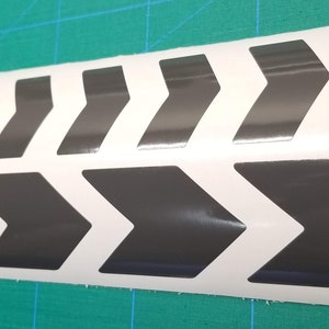 May include: A white vinyl sticker with a repeating pattern of black chevron arrows. The arrows are pointing to the right.