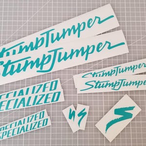 May include: A set of teal blue vinyl decals for a bicycle. The decals include the words "Specialized" and "Stumpjumper".