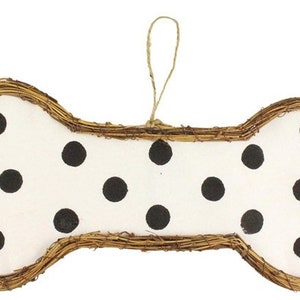 May include: A dog bone-shaped decoration with a white background and black polka dots. The bone is framed with woven brown twigs and has a twine loop for hanging. A charming accent for pet lovers.